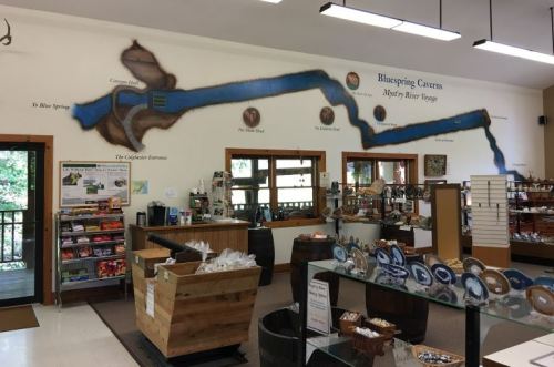 Interior of a visitor center with a wall map of Blue Spring Caverns, displays of souvenirs, and a welcoming atmosphere.