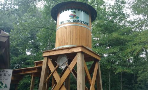 A wooden water tower with a sign for "Mystery River Mining Company" surrounded by trees.