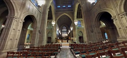 Interior of a grand church featuring high arches, stained glass windows, and rows of wooden pews.