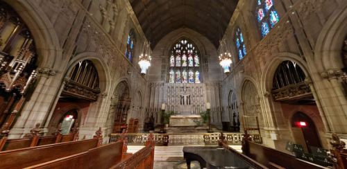 Interior of a grand church featuring stained glass windows, ornate stonework, and a grand piano in the foreground.