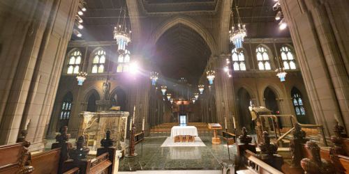 Interior of a grand cathedral featuring a central altar, ornate lighting, and tall stone arches.