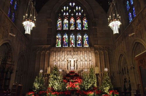 Interior of a church featuring stained glass windows, a decorated altar with flowers, and festive lighting.