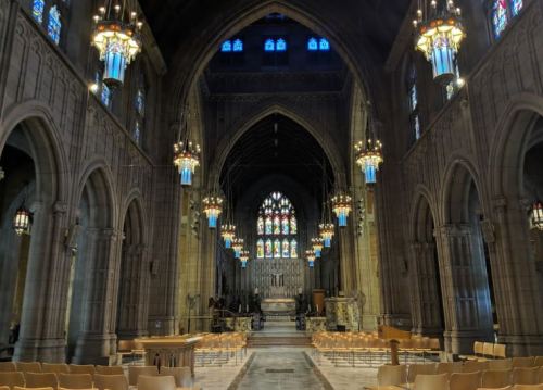 Interior of a grand cathedral featuring stained glass windows, ornate chandeliers, and wooden seating.