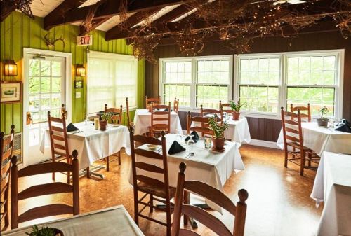 Cozy restaurant interior with wooden chairs, white tablecloths, and large windows letting in natural light.