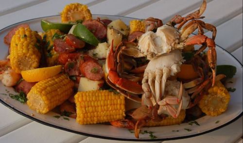 A colorful seafood platter featuring crab, corn, sausage, potatoes, and lime, garnished with herbs.