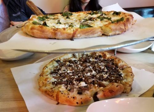 Two pizzas on a serving tray: one topped with spinach and cheese, the other with mushrooms and feta.