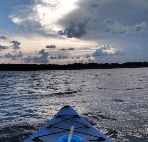 A kayak on calm water, with a dramatic sky filled with clouds at sunset.