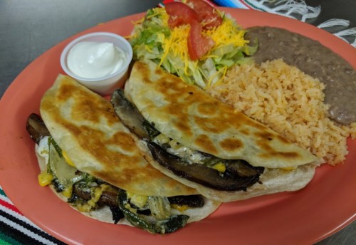 A colorful plate featuring two quesadillas, rice, refried beans, salad, and a side of sour cream.