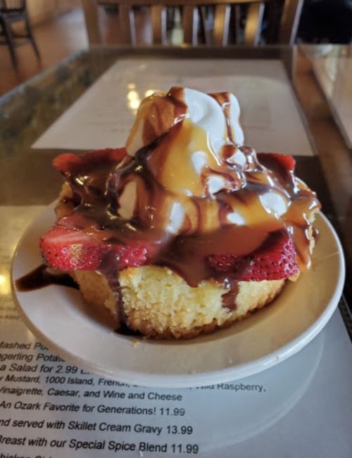 A dessert featuring a cupcake topped with ice cream, strawberries, and drizzled with chocolate sauce.