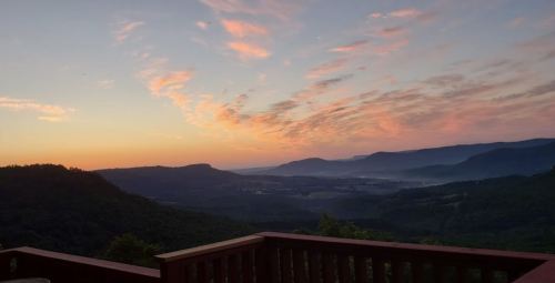 A serene sunset over rolling hills, with pink and orange clouds illuminating the sky.