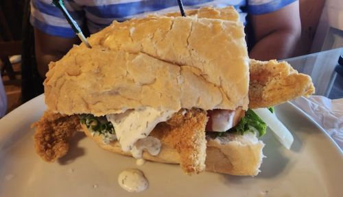 A large sandwich filled with fried seafood, lettuce, and sauce, served on a plate with a side of napkins.