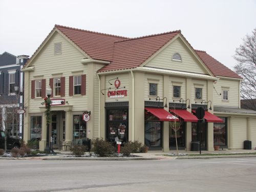 A charming two-story building with a red-tiled roof, featuring storefronts and festive decorations.