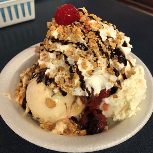 A bowl of ice cream topped with whipped cream, chocolate syrup, crushed nuts, and a cherry.