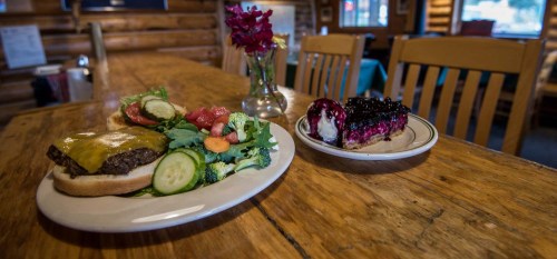 A plate with a cheeseburger and a fresh salad, alongside a dessert of berry pie, on a rustic wooden table.