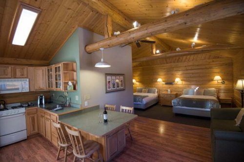 Cozy cabin interior featuring a kitchen, dining area, and two beds with wooden accents and warm lighting.