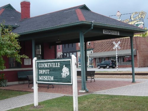 Historic Cookeville Depot Museum with a sign, benches, and nearby railroad tracks under a cloudy sky.