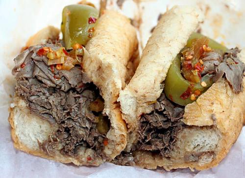 A close-up of a sliced sandwich filled with tender beef, jalapeños, and spices on a soft bread roll.