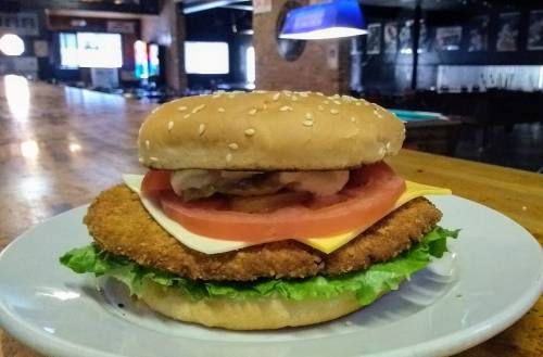 A large sesame seed burger with lettuce, tomato, cheese, and a crispy chicken patty on a white plate.