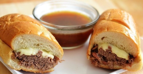 Two beef sandwiches with melted cheese, served alongside a small bowl of dipping broth.