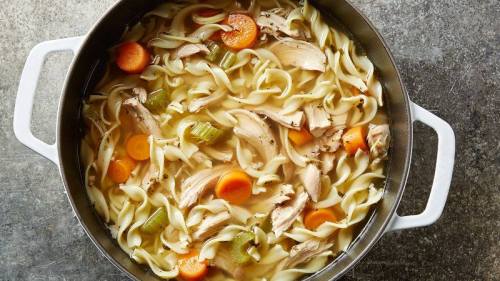 A pot of chicken noodle soup with noodles, carrots, celery, and pieces of chicken in a savory broth.
