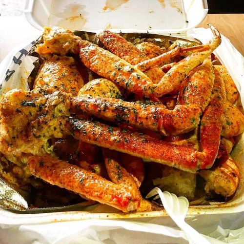 A takeout container filled with seasoned crab legs and seafood, garnished with herbs and spices.