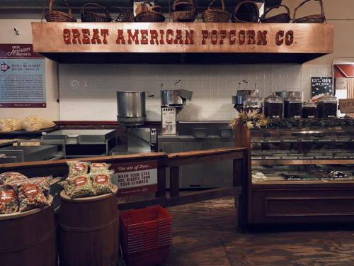 Interior of a popcorn shop with a sign reading "Great American Popcorn Co." and various popcorn flavors displayed.