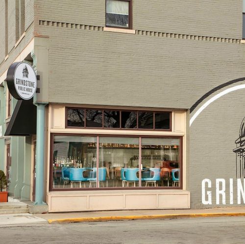 Exterior view of a public house with large windows showcasing colorful seating and a sign reading "Grindstone Public House."