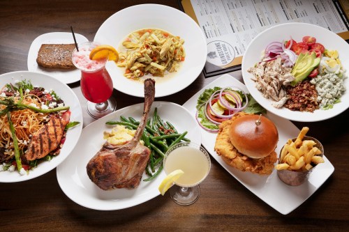 A variety of dishes including grilled chicken, pasta, salad, a burger, and drinks arranged on a table.