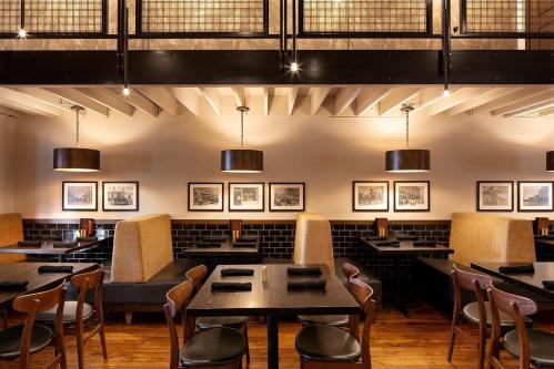 Modern restaurant interior with wooden tables, leather seating, and framed artwork on the walls. Warm lighting enhances ambiance.