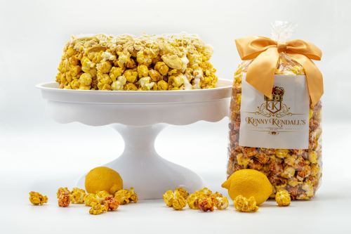 A cake made of popcorn on a white pedestal, next to a bag of popcorn with a bow and scattered popcorn pieces.