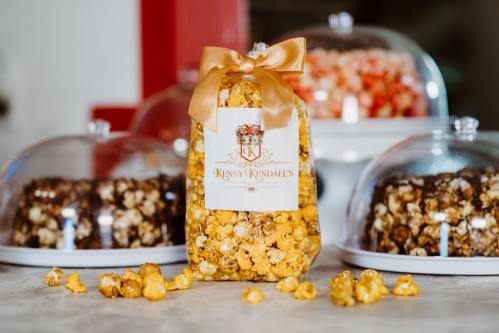 A bag of yellow popcorn tied with a ribbon, with colorful popcorn varieties displayed under glass domes in the background.