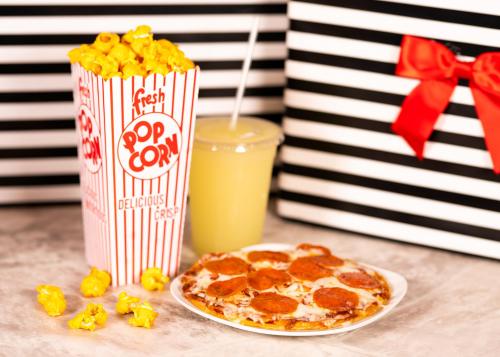 A striped popcorn box, a plate of pepperoni pizza, and a drink sit on a table with striped gift boxes in the background.