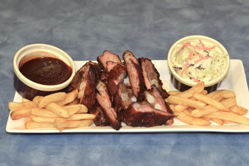 A plate of smoked ribs with barbecue sauce, French fries, and coleslaw on a blue background.