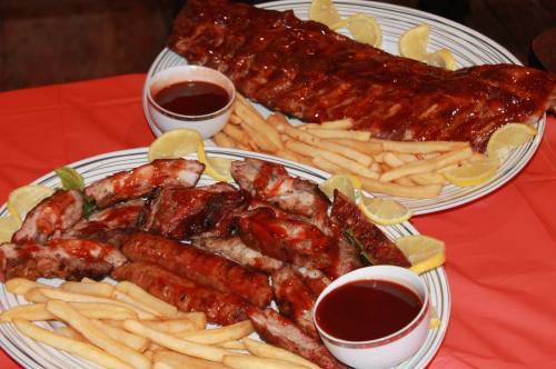 Two platters of barbecue ribs with fries and lemon wedges, accompanied by dipping sauces.