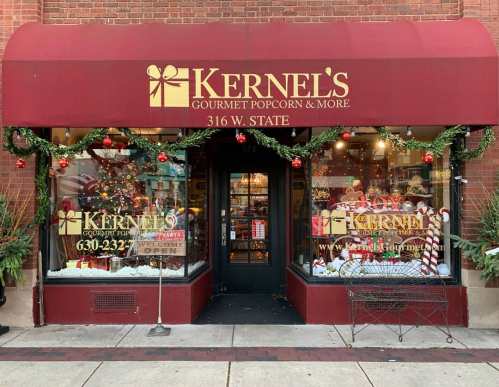 A festive storefront of Kernel's Gourmet Popcorn, decorated with holiday garlands and lights.