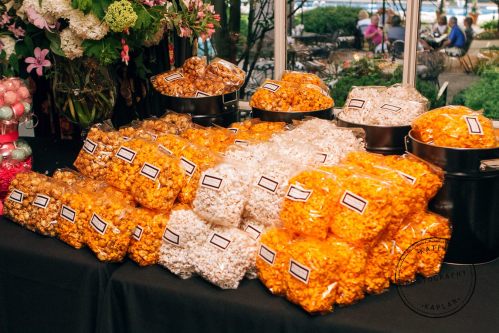 A display of colorful popcorn bags in various flavors, arranged neatly on a table with flowers in the background.