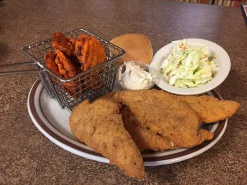 A plate of fried fish fillets, sweet potato fries in a basket, coleslaw, and a bun with dipping sauce.