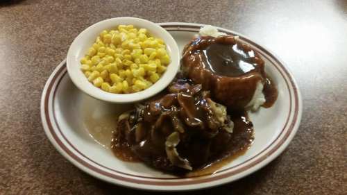 A plate of meatloaf with gravy, mashed potatoes, and a side of corn.