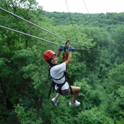 A person in a red helmet zip-lining through a lush green forest, smiling and enjoying the adventure.