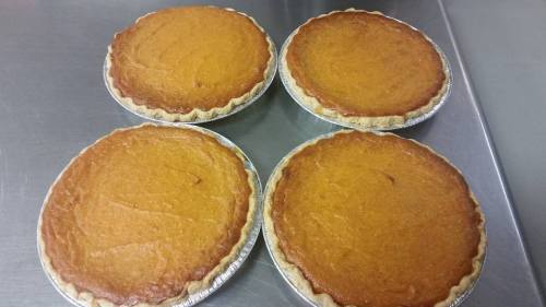 Four freshly baked pumpkin pies on a silver baking tray.