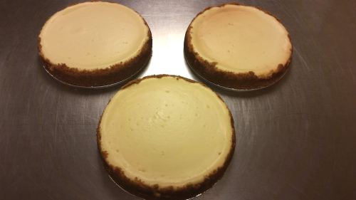Three round cheesecakes with golden crusts on a silver surface.