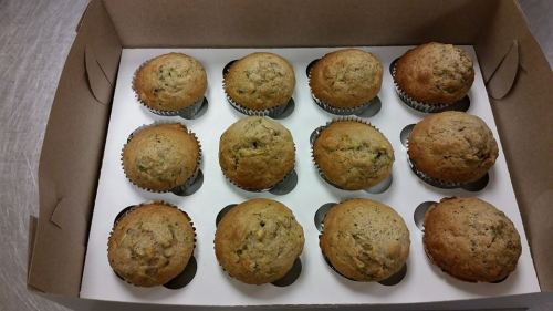 A box containing twelve freshly baked muffins, arranged in two rows, with a light brown color and a textured top.