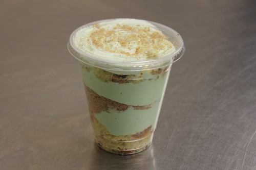 A clear cup filled with layers of mint green dessert and crumbled cake, topped with a light sprinkle.