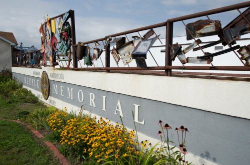 A colorful memorial featuring various objects and signs, surrounded by flowers and a cloudy sky.