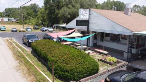 A pizza restaurant with colorful awnings, surrounded by greenery and parked cars on a sunny day.