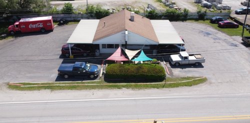 Aerial view of a building with a brown roof, colorful tents, parked cars, and a Coca-Cola truck nearby.