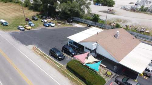 Aerial view of a parking lot with cars and a building, featuring colorful canopies and a grassy area nearby.