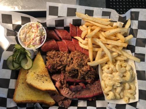 A platter of barbecue featuring brisket, pulled pork, sausage, fries, coleslaw, macaroni, pickles, and toast.