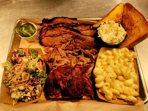 A tray of barbecue featuring brisket, pulled pork, chicken, macaroni and cheese, coleslaw, salad, and toast.