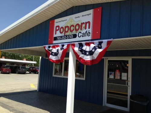 Exterior of a blue building with a sign reading "Popcorn Café" and patriotic bunting decorations.